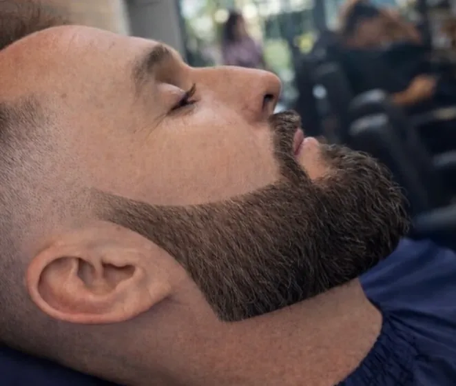 Perfil de cliente reclinado, com a barba cheia alinhada e o contorno marcado junto ao rosto.