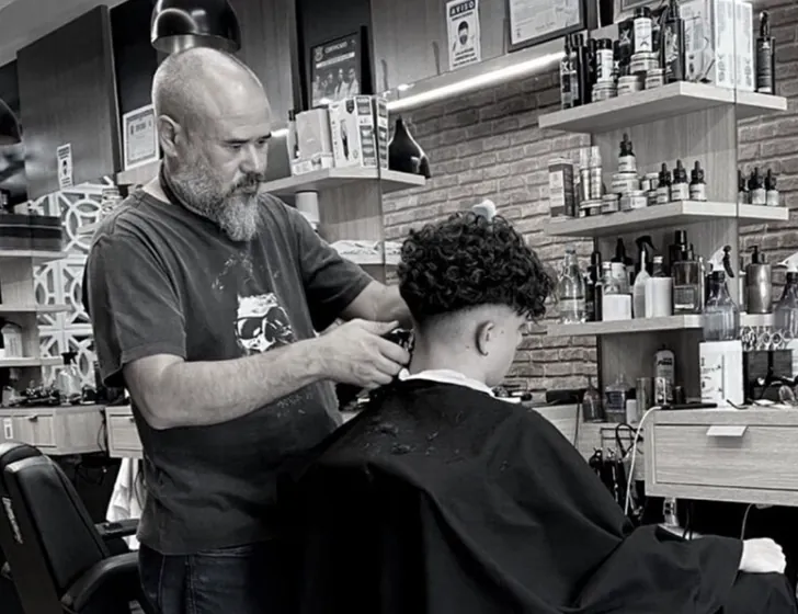 Fotografia em preto e branco: máquina passando na nuca de um cliente de cabelo cacheado.