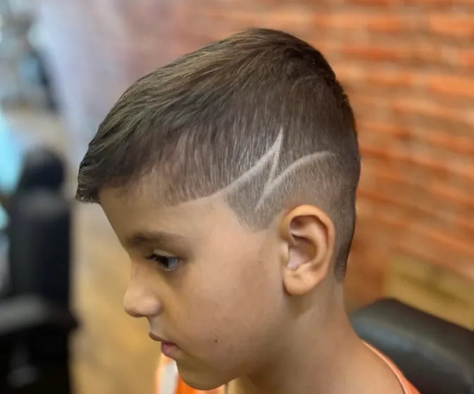 Corte infantil com degradê e um risco desenhado na lateral da cabeça.