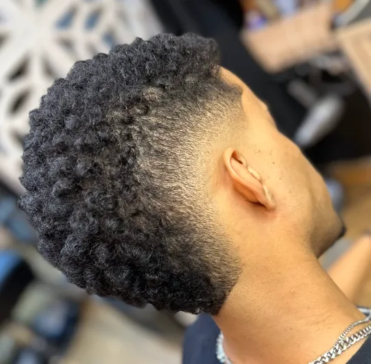 Cabelo crespo volumoso no topo, com degradê fechado na lateral e na nuca.